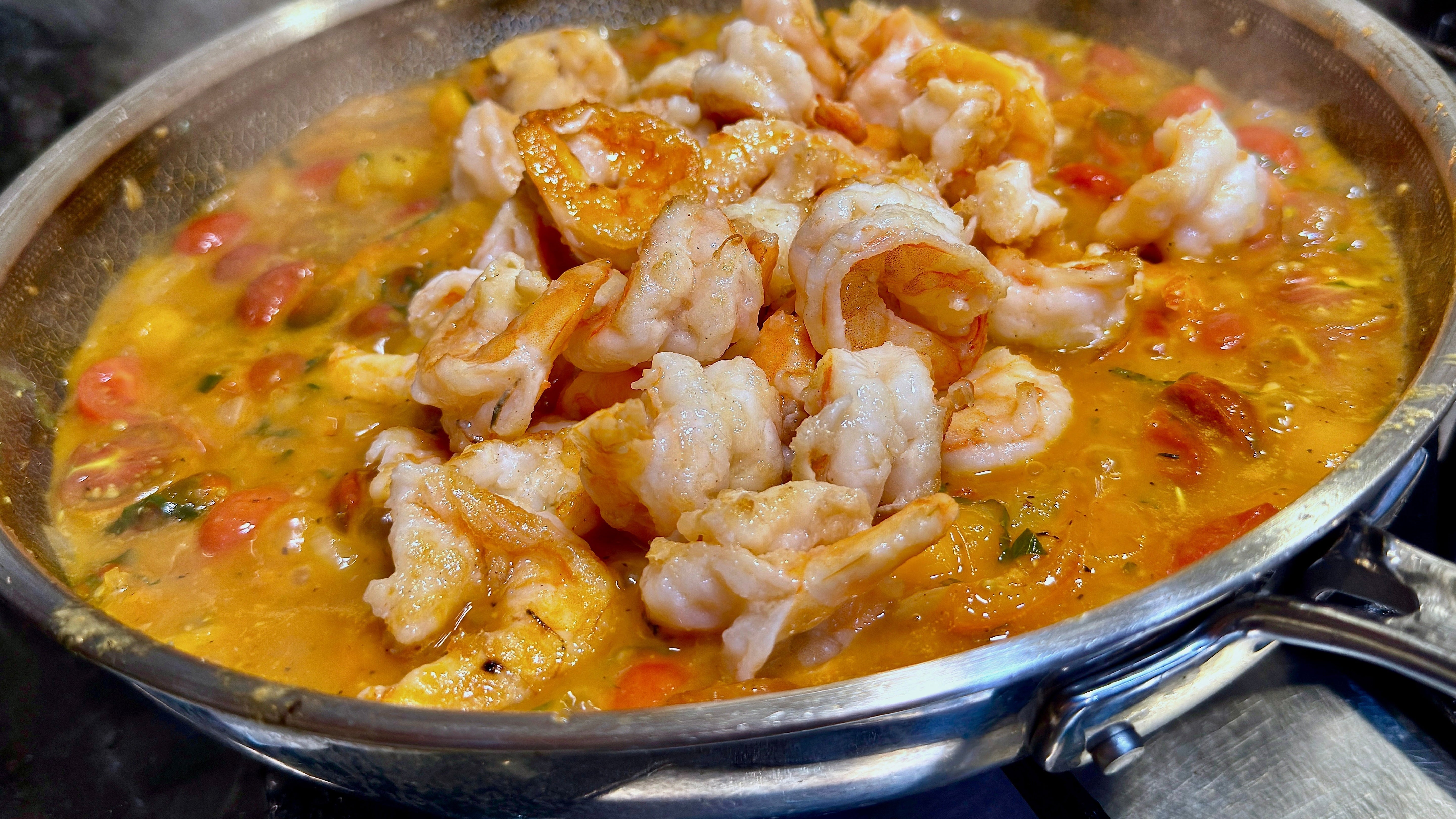Poached shrimp has just been added to a 12" pan filled with a cherry tomato white wine sauce