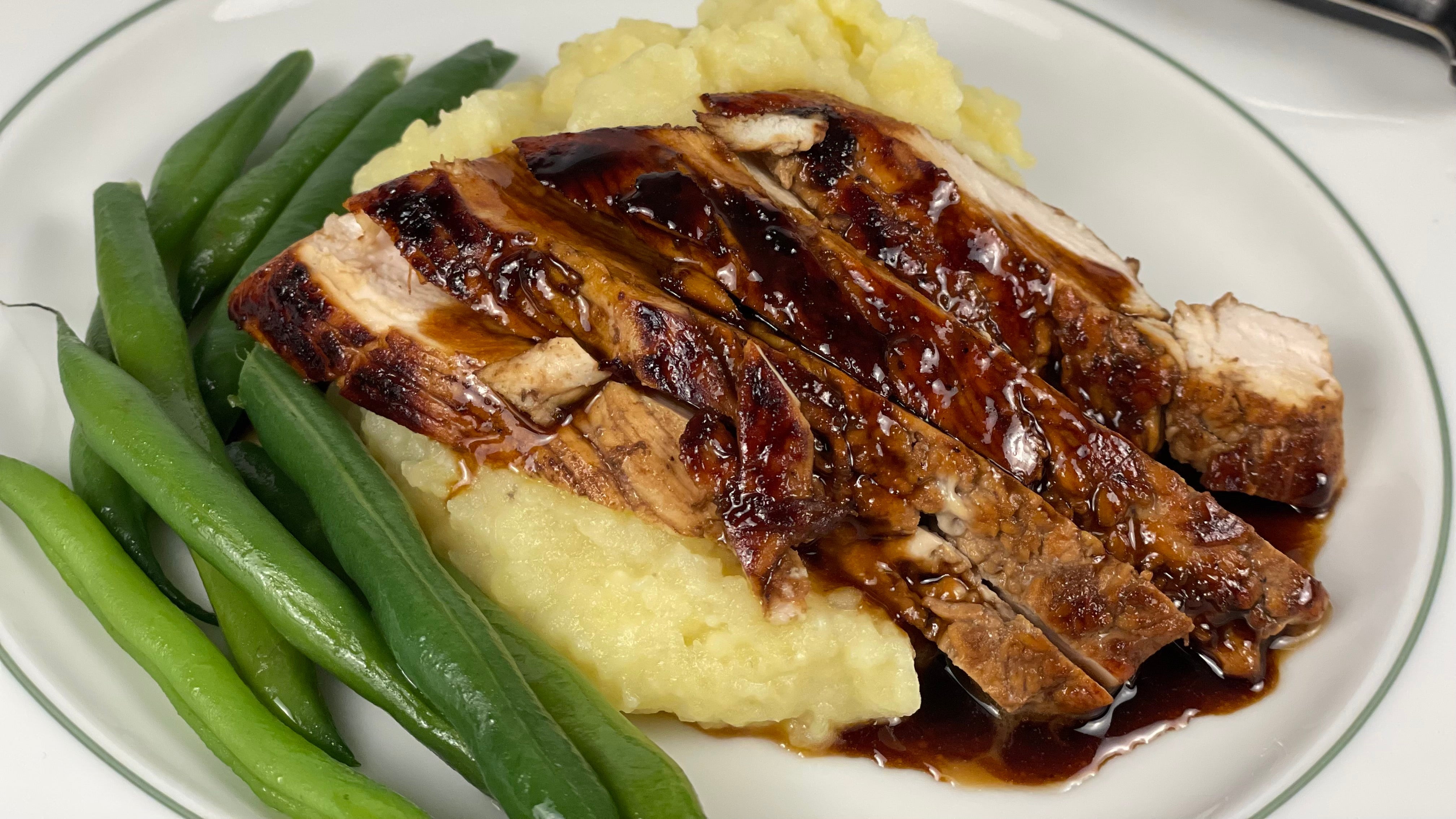 Sliced chicken is nestled in a bed of olive oil mashed potatoes and accompanied with green beans, a rich butter balsamic sauce covers the chicken.
