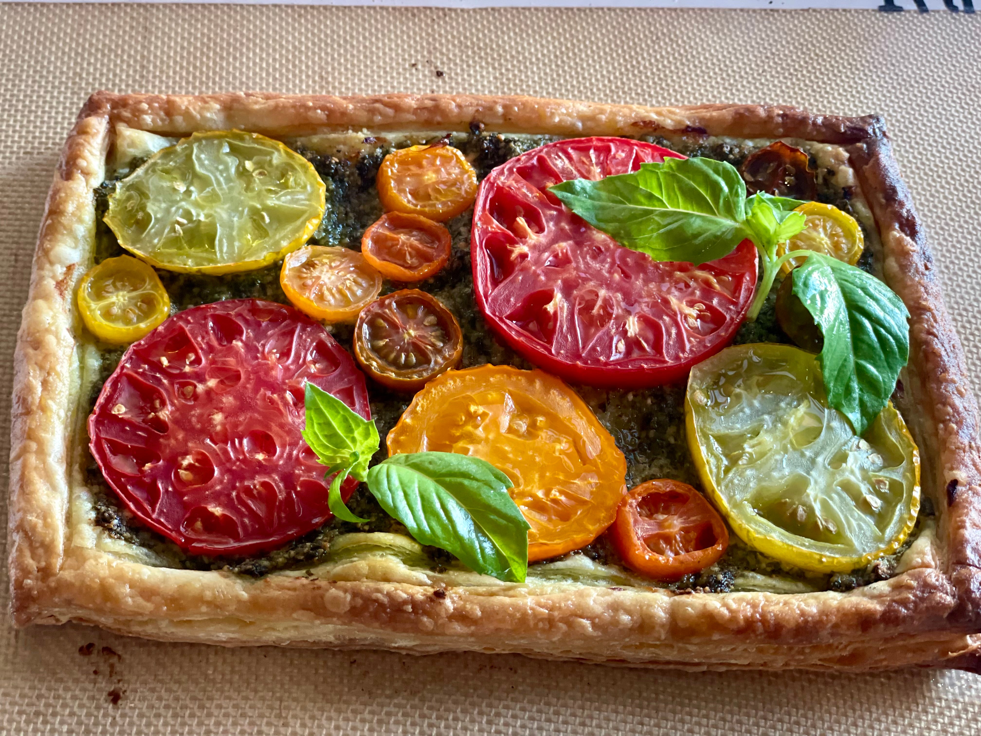 Sliced tomatoes of many different sizes and flavors are nestled into fresh pesto and baked into a rectangular tart made of puff pastry