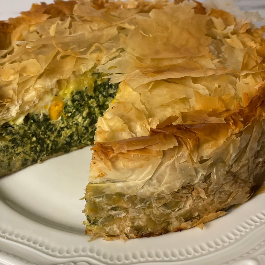 An 8" "Torta Pasqualina" savory eggy cake is topped with crispy phyllo and shown on a fancy porcelain plate. One slice has been removed.