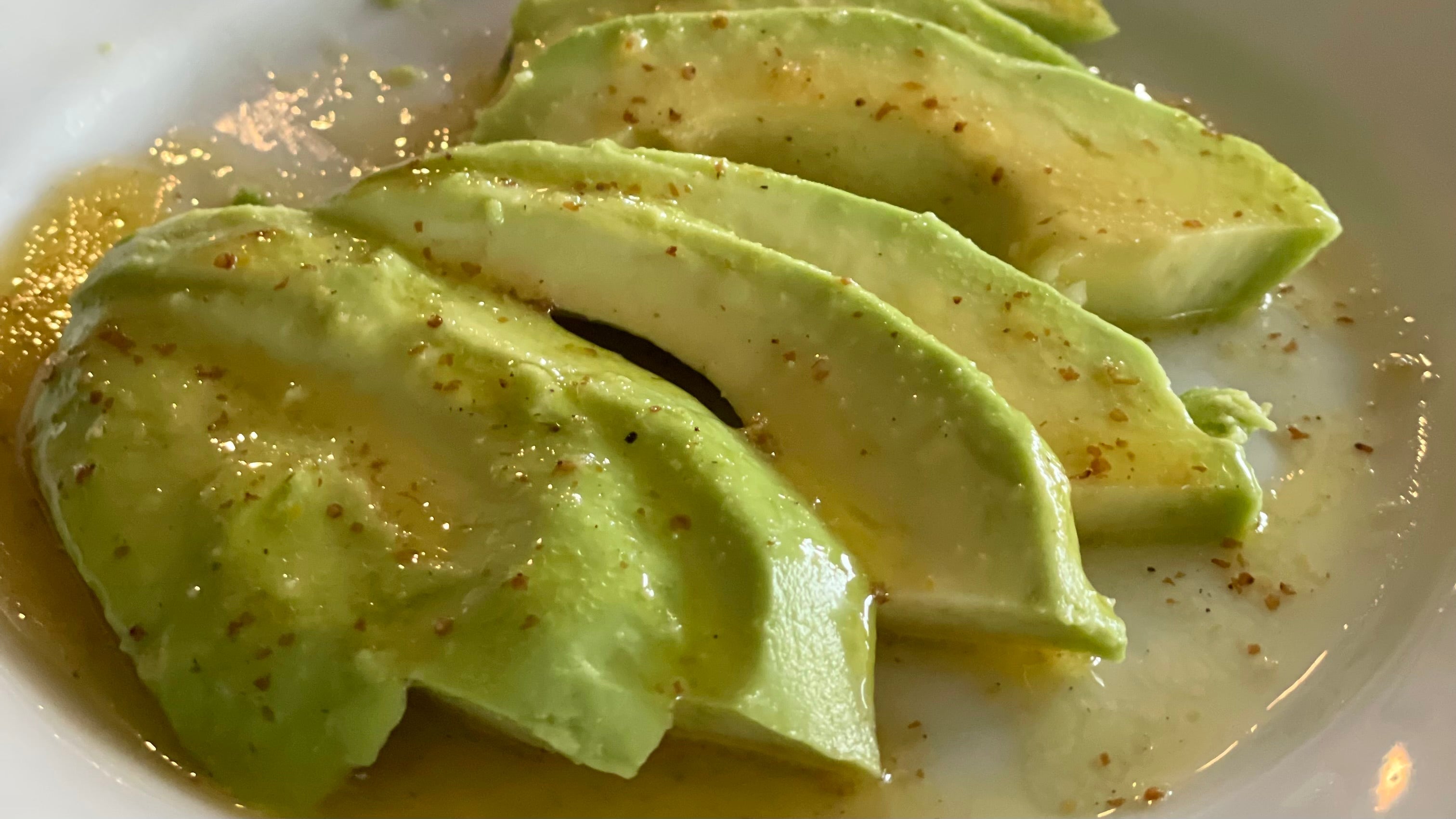 Sliced avocados are arranged on a simple porcelain plate and drenched in a lemon olive oil and rosé balsamic vinegar dressing.