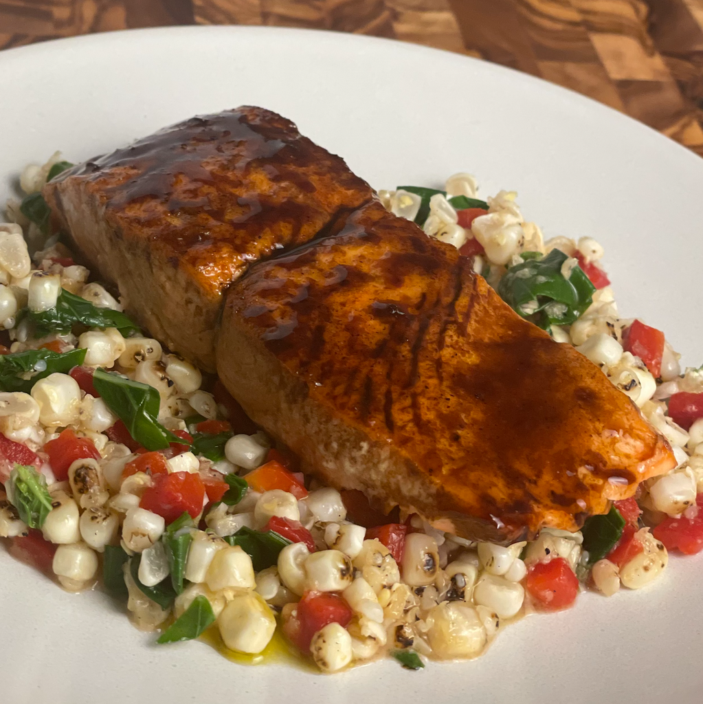 A 3 oz grilled salmon steak with balsamic olive oil glaze rests atop a charred corn salsa