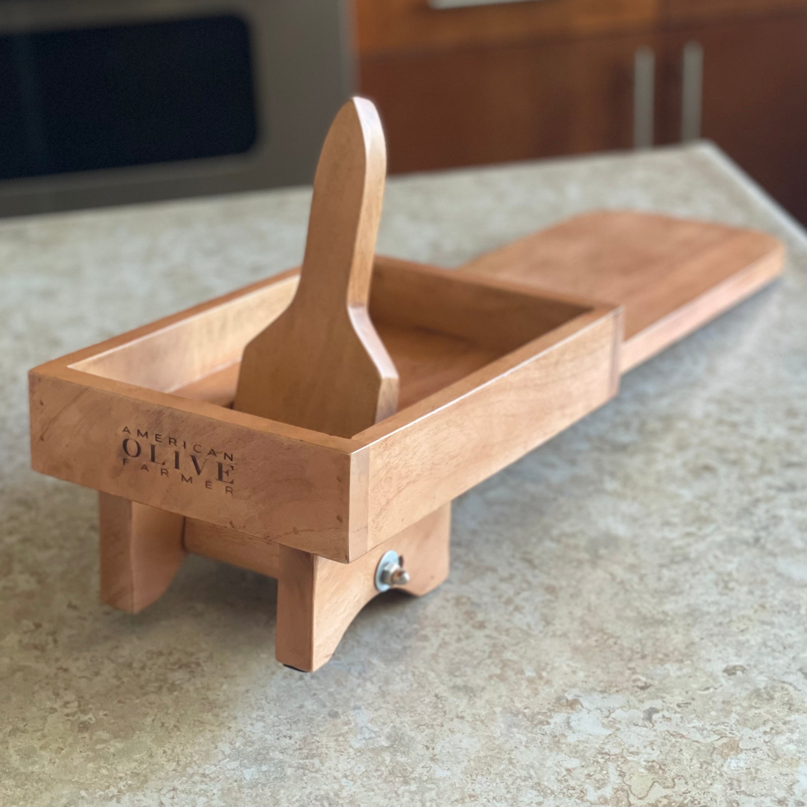 ¾ view of a manual wooden olive crusher from the front. The paddle is pushed away from the viewer in the closed / crushing position.