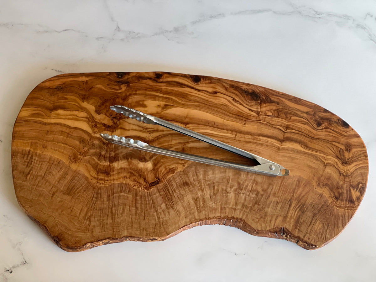 Large olivewood board with metal tongs on a marble surface
