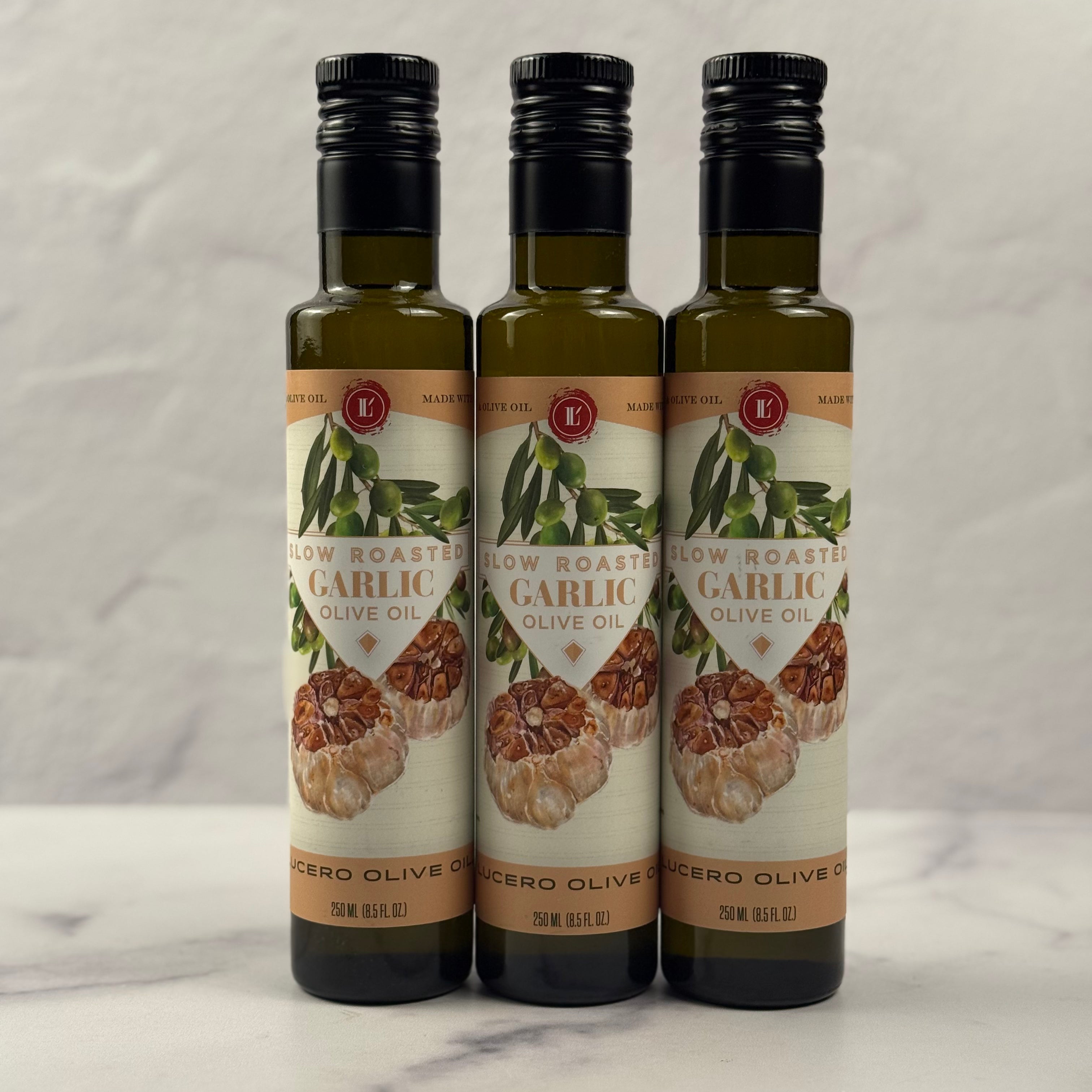 Three 250 ml bottles of Lucero Garlic Olive Oil are shown in a marble kitchen.