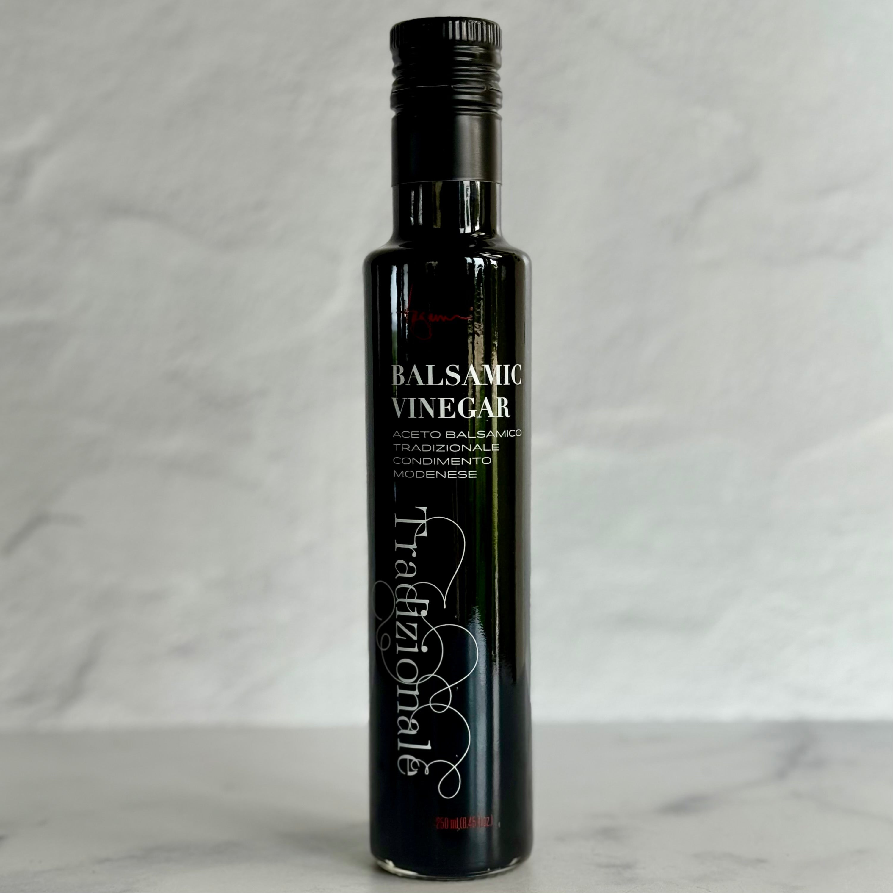 A single 250 ml bottle of balsamic vinegar sits on a marble counter with a Tuscan plaster wall behind it