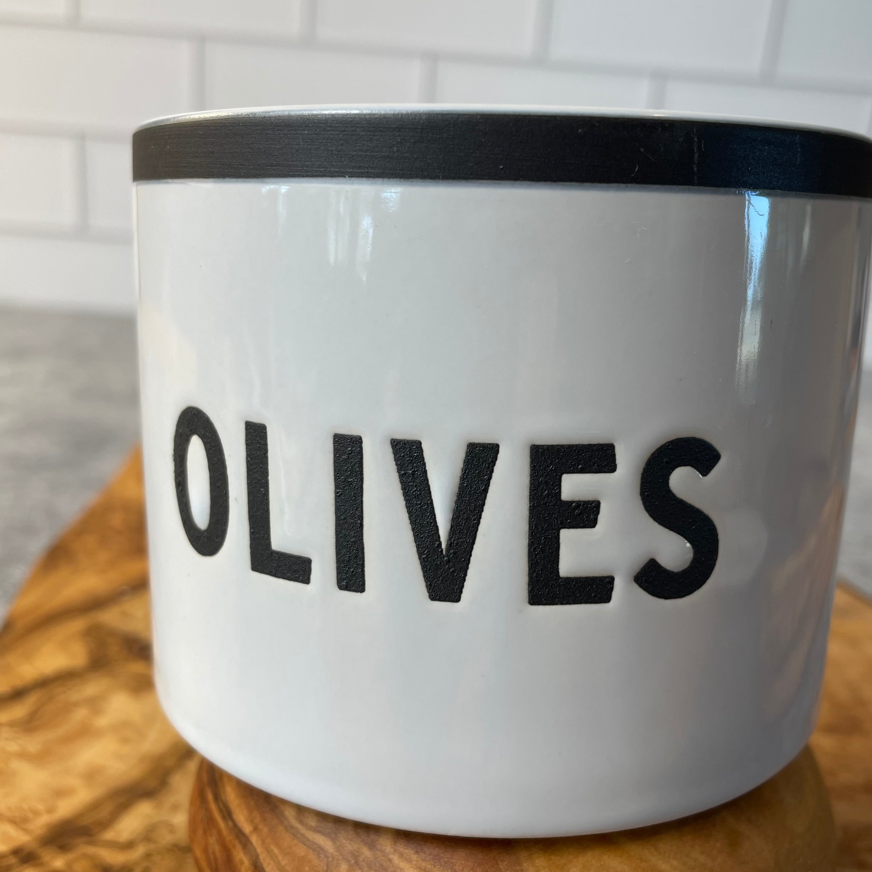 Close up image of a straight sided round bowl marked OLIVES in resist glaze. The main body is shiny and smooth, the word olives is matte and rough. There is a tasteful line around the rim that is also matte and rough.