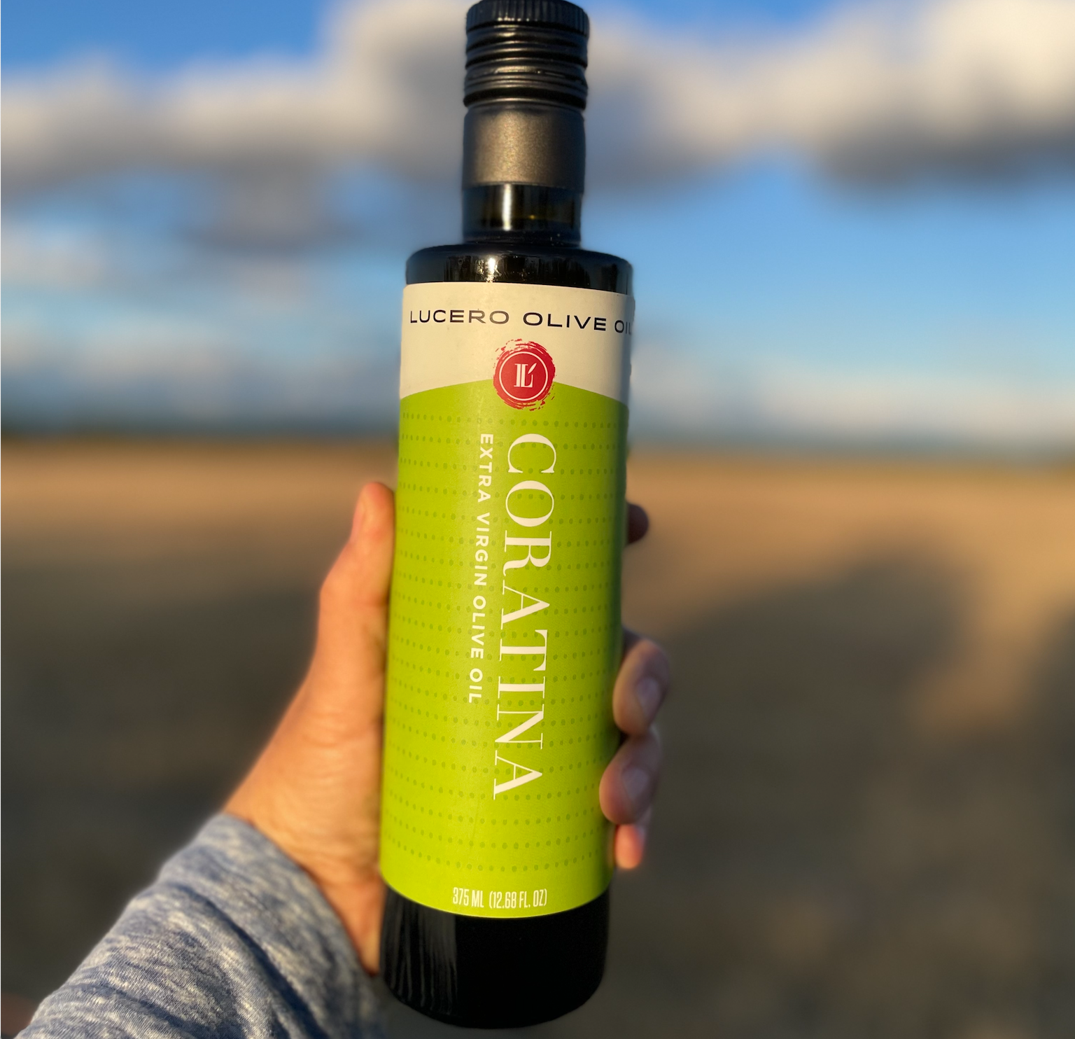 Liz holds a bottle of Coratina at arm's length to capture its design with the golden light of dusk in front of a dry-farmed pasture.