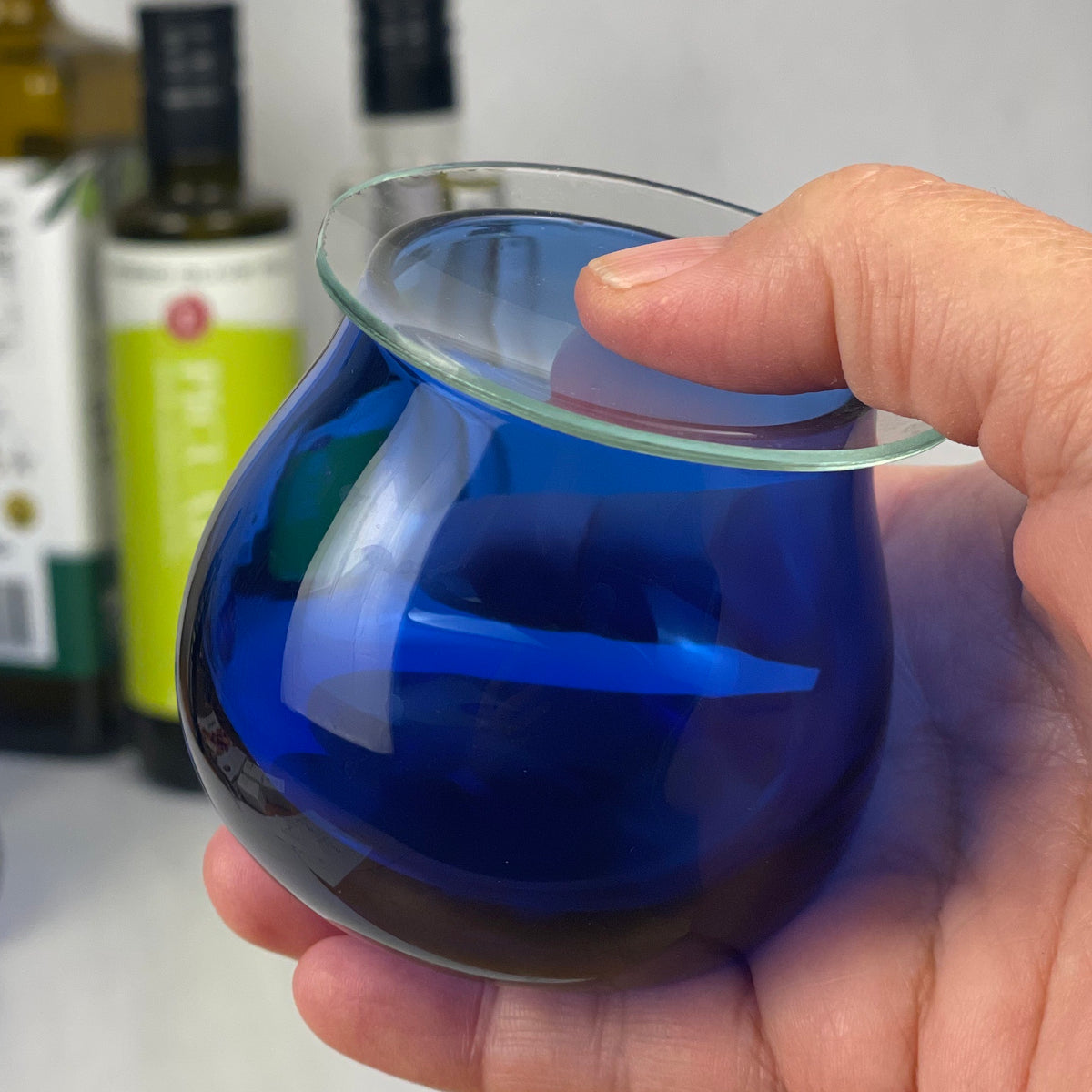An olive oil tasting glass with watch glass lid is cradled in someone's right hand.