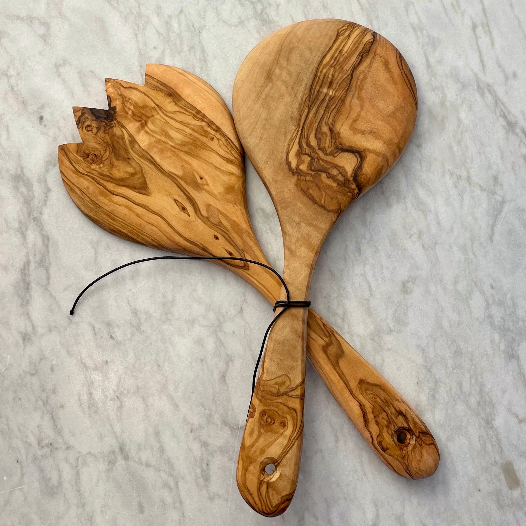 A pair of olive wood salad servers is shown facedown with a black cord holding them together