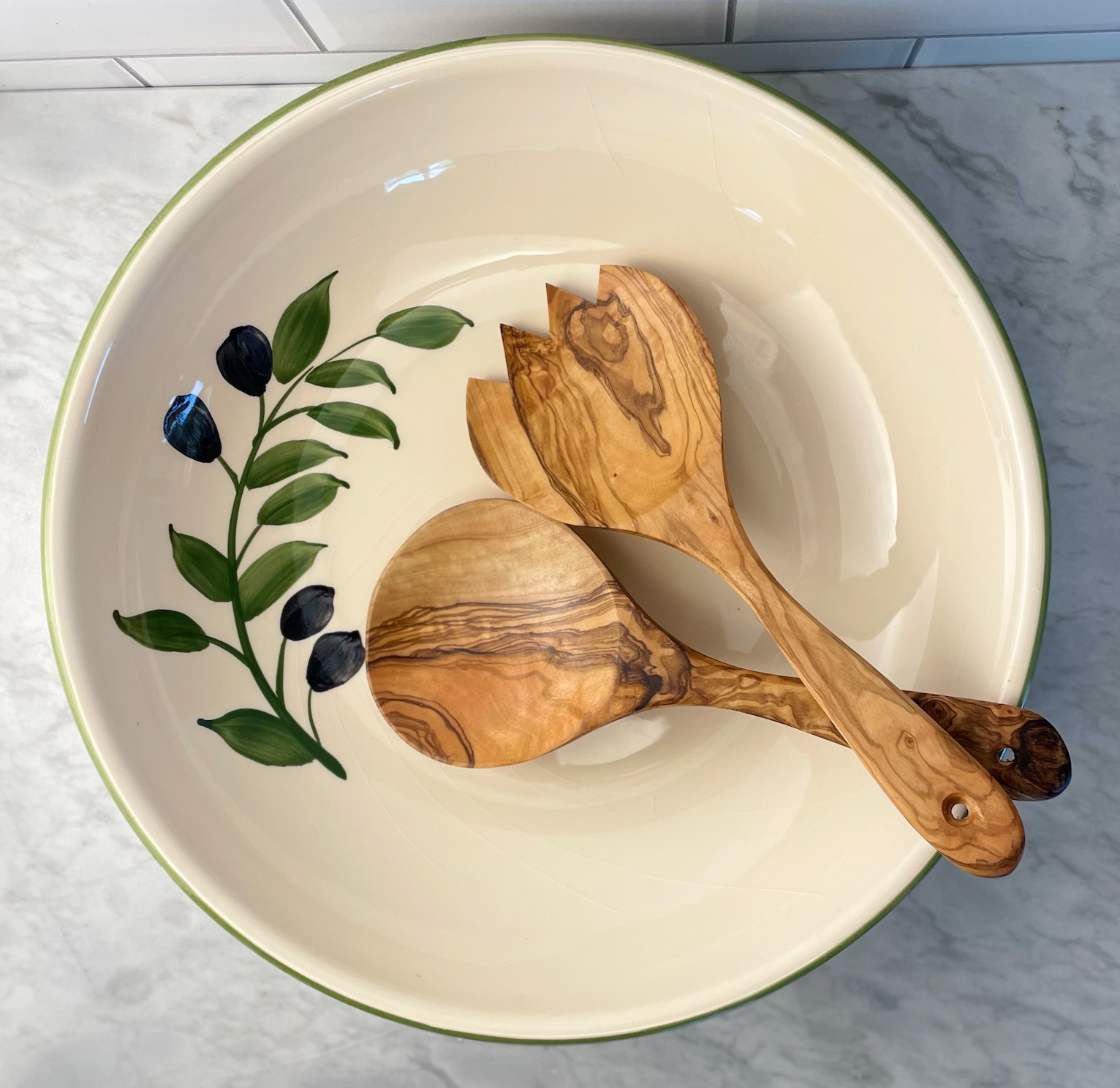 Pair of olive wood salad servers shown in a ceramic salad bowl painted with an olive branch motif