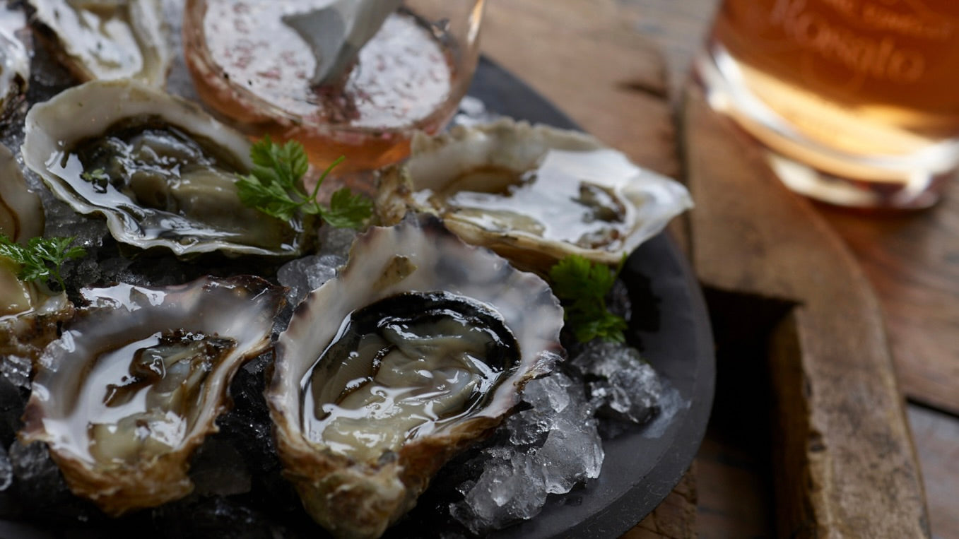 Oysters on the half shell are shown with a Tagami Rosato Balsamic Vinegar Mignonette Sauce. A bottle of Rosato Balsamic Vinegar is subtly in the background