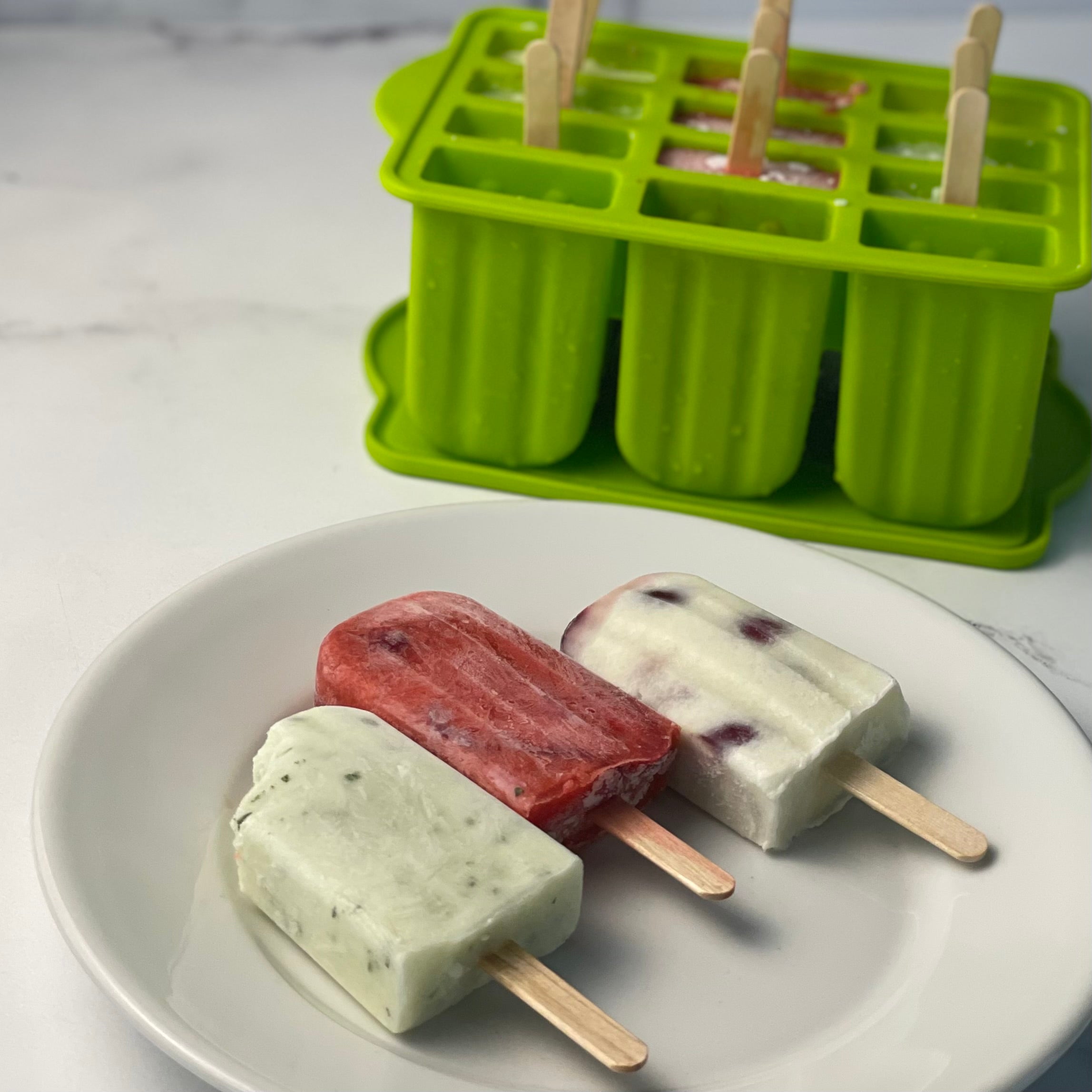 Cucumber Mint, Strawberry Ascolano Daiquiri, and Cherries & Cream Paletas shown on a plate with a 12 section ice pop maker in the background