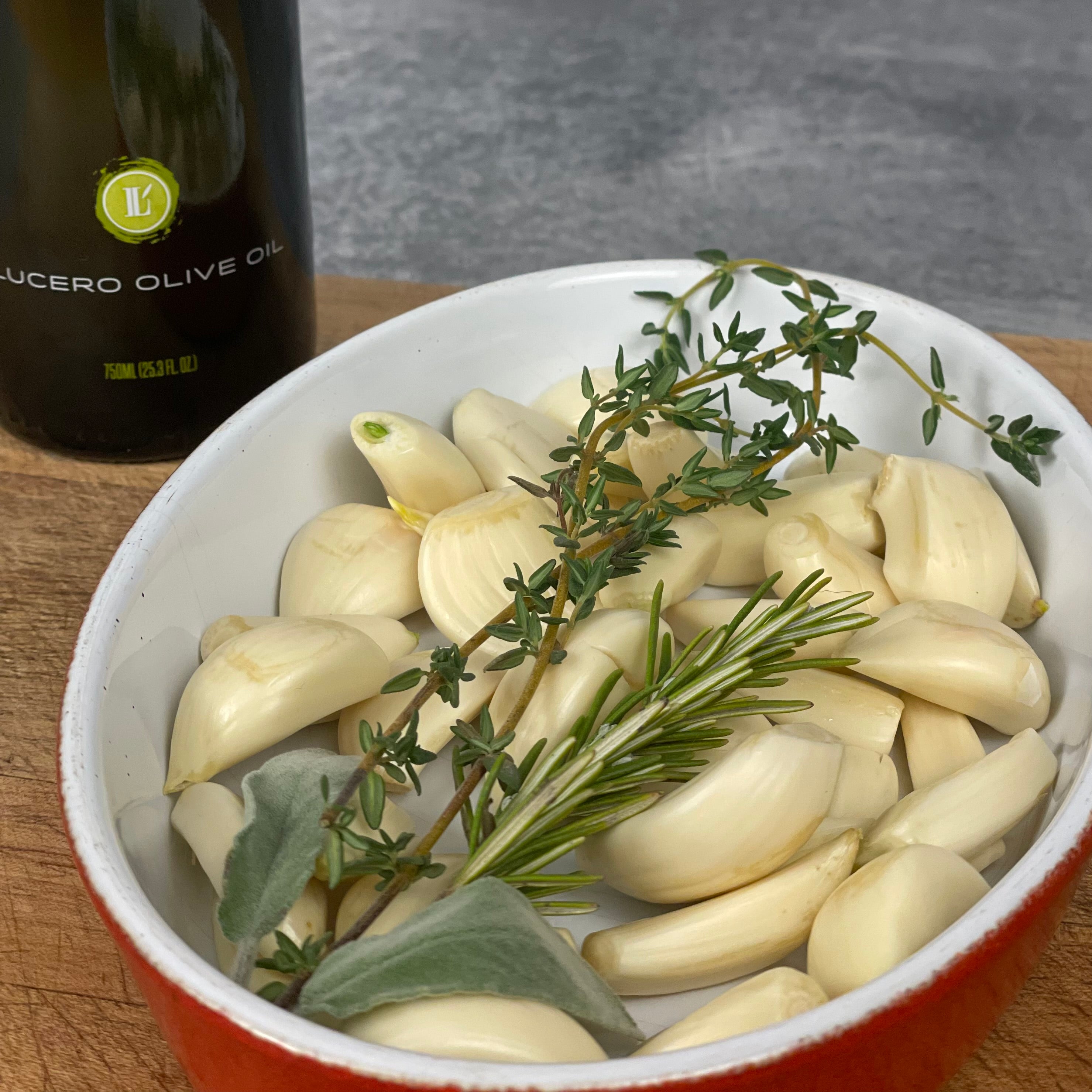 Donald pours Lucero Arbequina EVOO into a small oval baker filled with peeled garlic cloves and herbs.