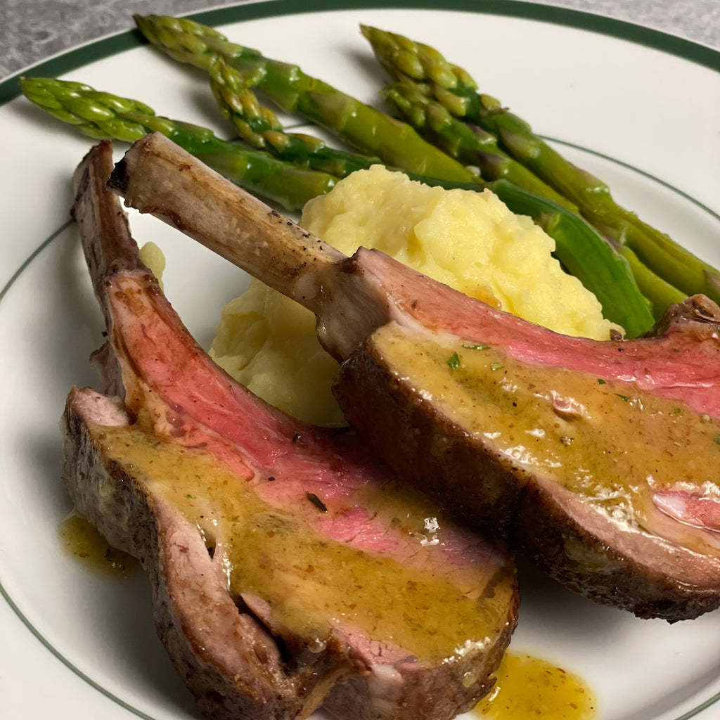 2 rare lamb chops, sauced, on a bed of mashed potatoes with fresh asparagus.