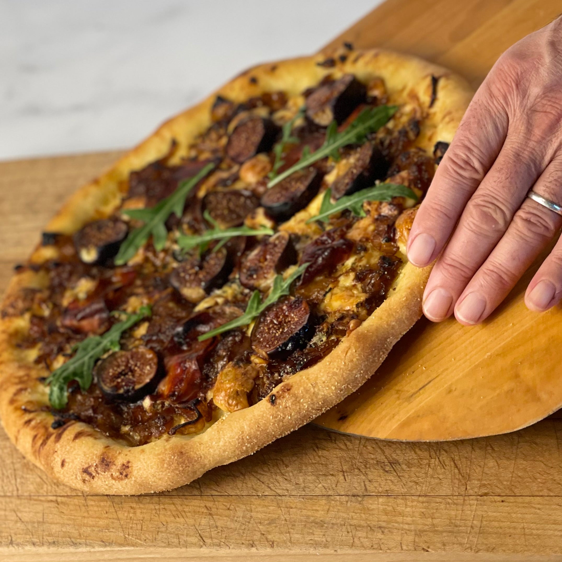 Donald slides a Fig and Gorgonzola pizza from a peel to a wooden cutting board