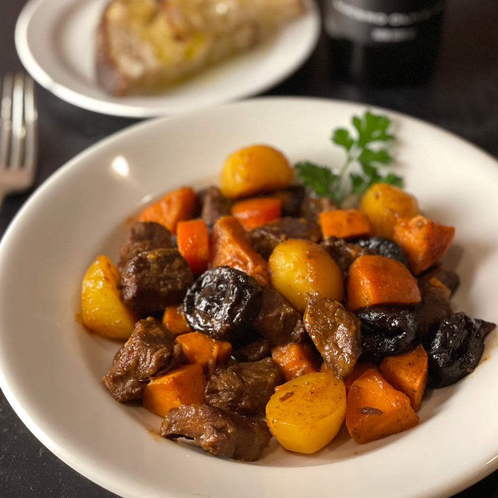 A French porcelain soup plate is filled with luscious roasted beef and stewed prunes, sweet potato, new potatoes, and carrots in a savory sauce.