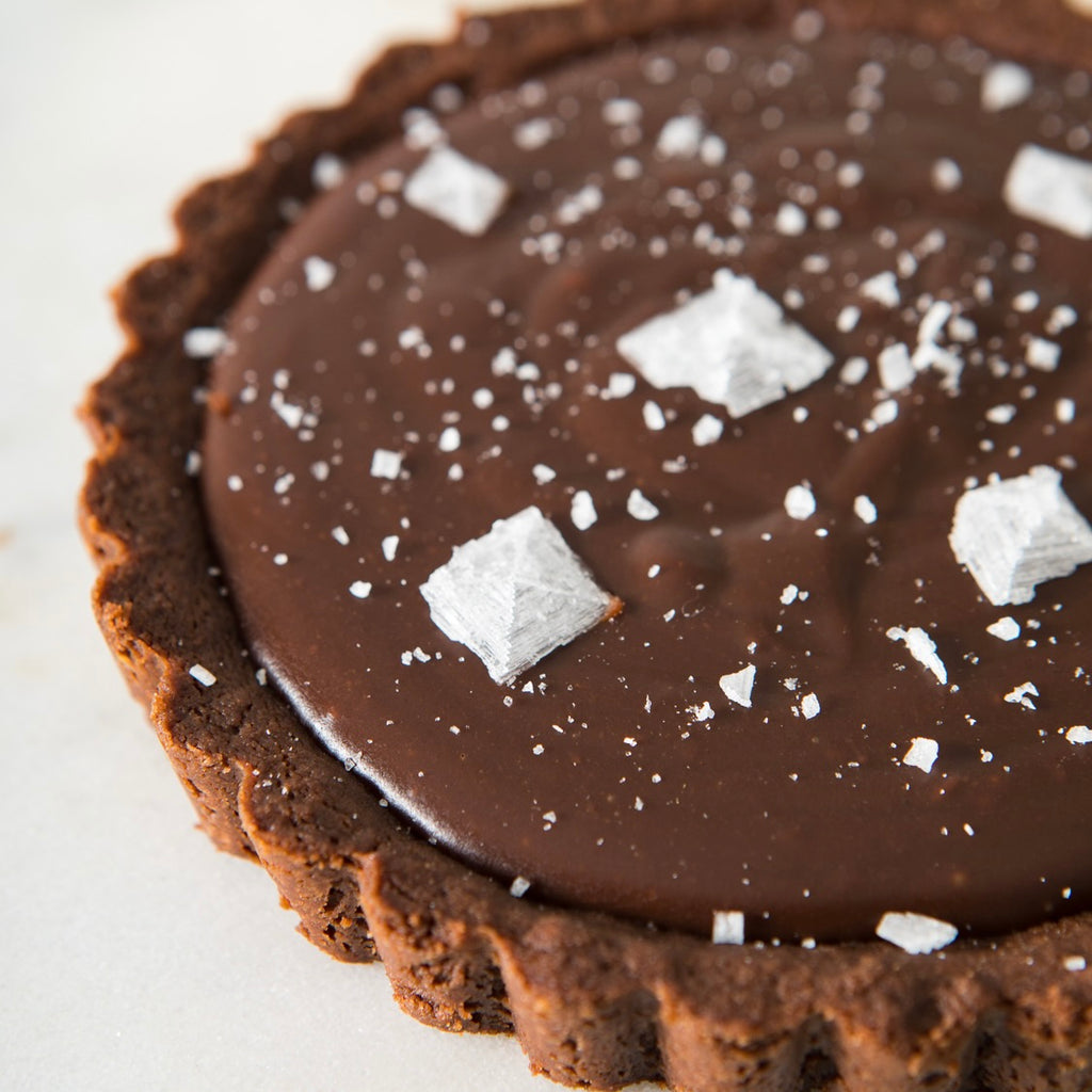 Close up image of a 4" tartlet with chocolate crust and smooth chocolatey filling, finished with pyramids and sprinkles of Jacobsen Salt.