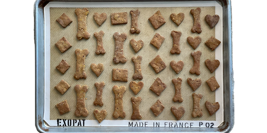 A professional weight half baking sheet is filled with small dog biscuits shaped like hearts, diamonds, squares, and "dog bones" rest on a silicone "exopat".