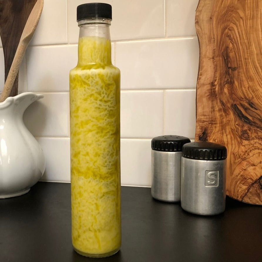 Congealed extra virgin olive oil in a clear glass 250 ml bottle on a kitchen counter.