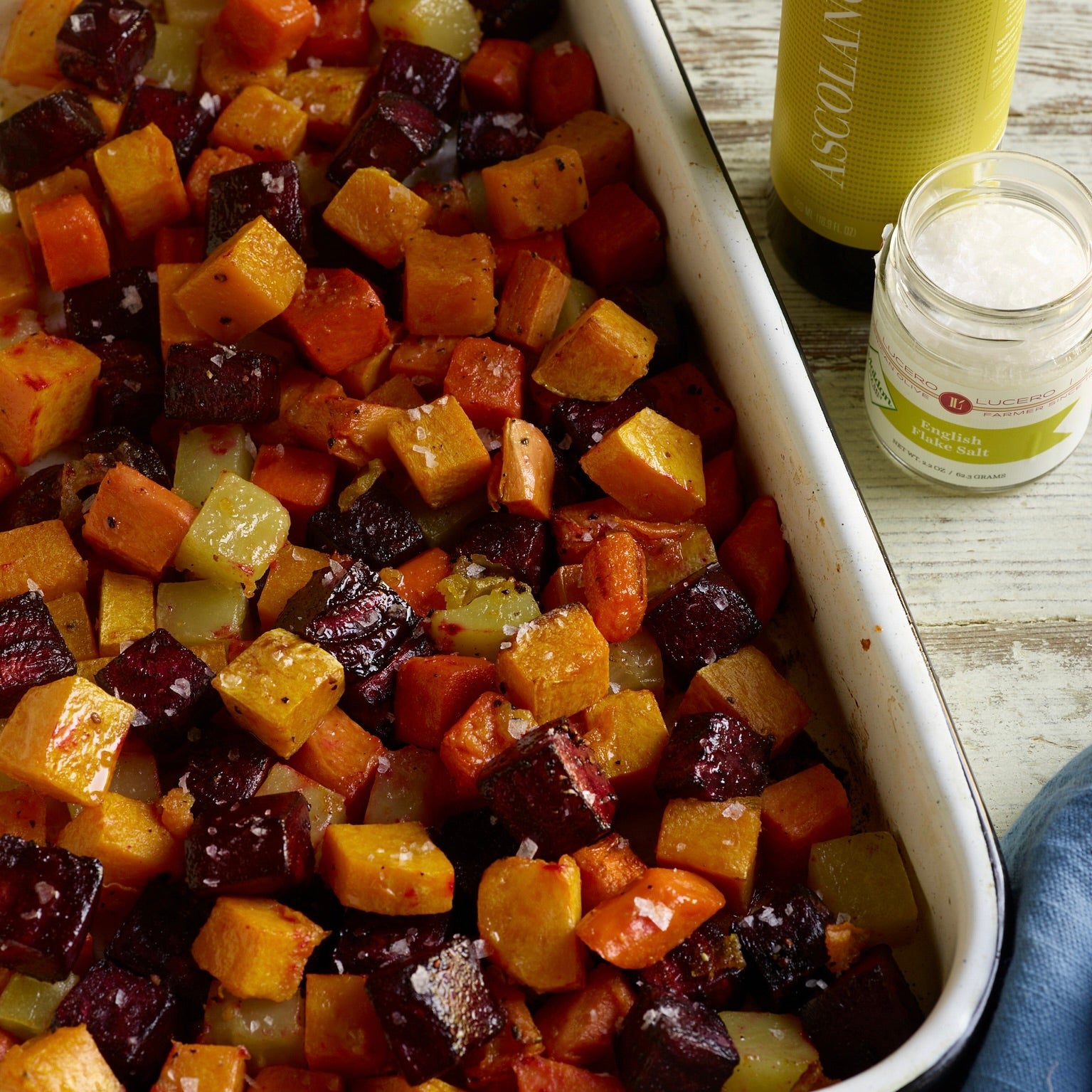 Roasted cubes of beets, potatoes, and other root vegetables glisten in an overhead image of a roasting pan.