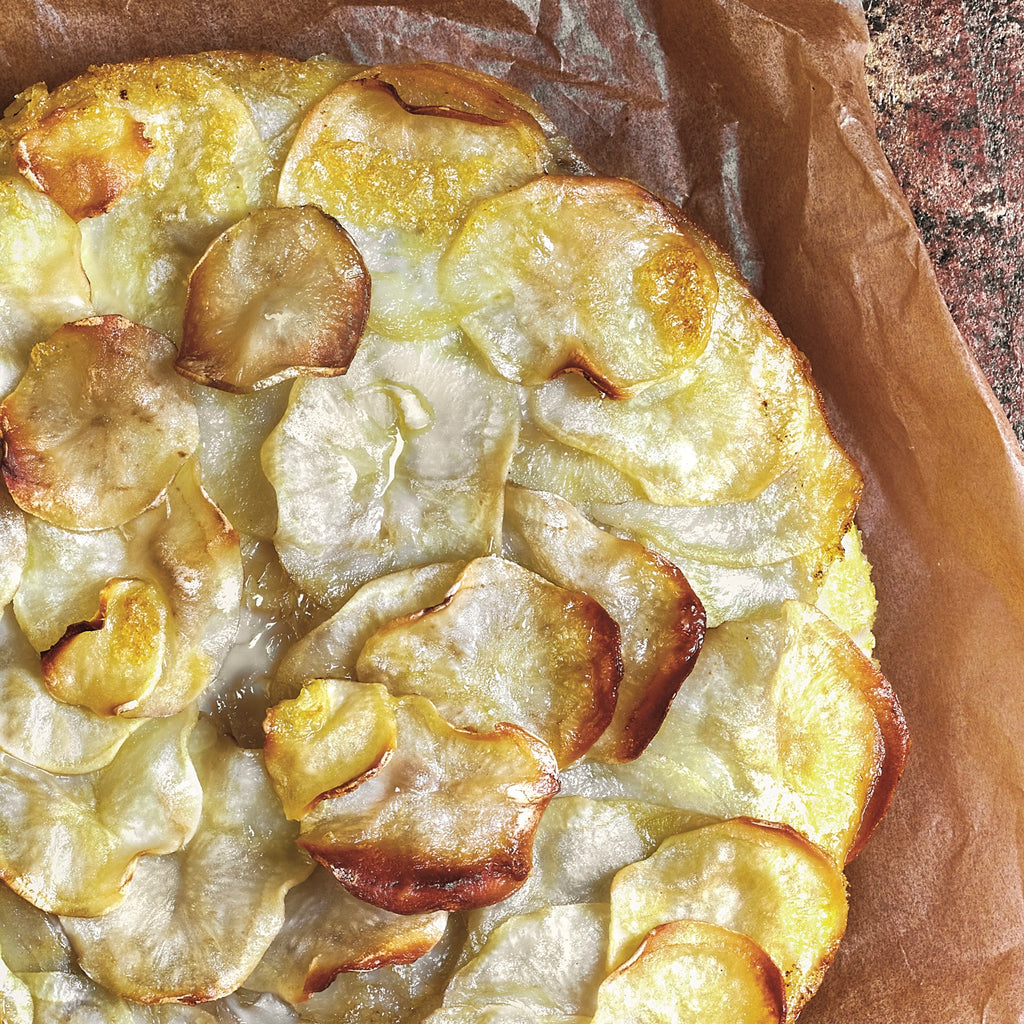 Thinly sliced potatoes are baked into a round shown with crisp, cooked edges on oily parchment paper.