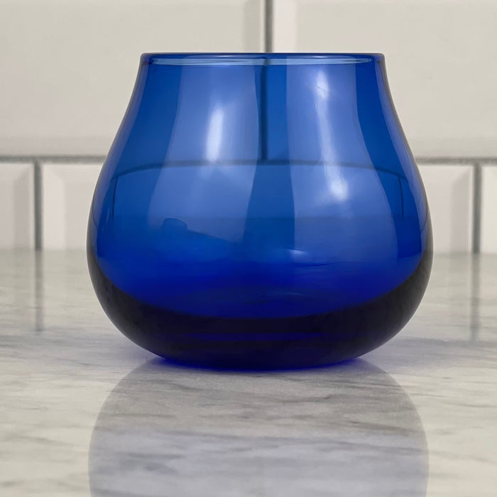 A single cobalt blue olive oil tasting glass rests on a marble board.
