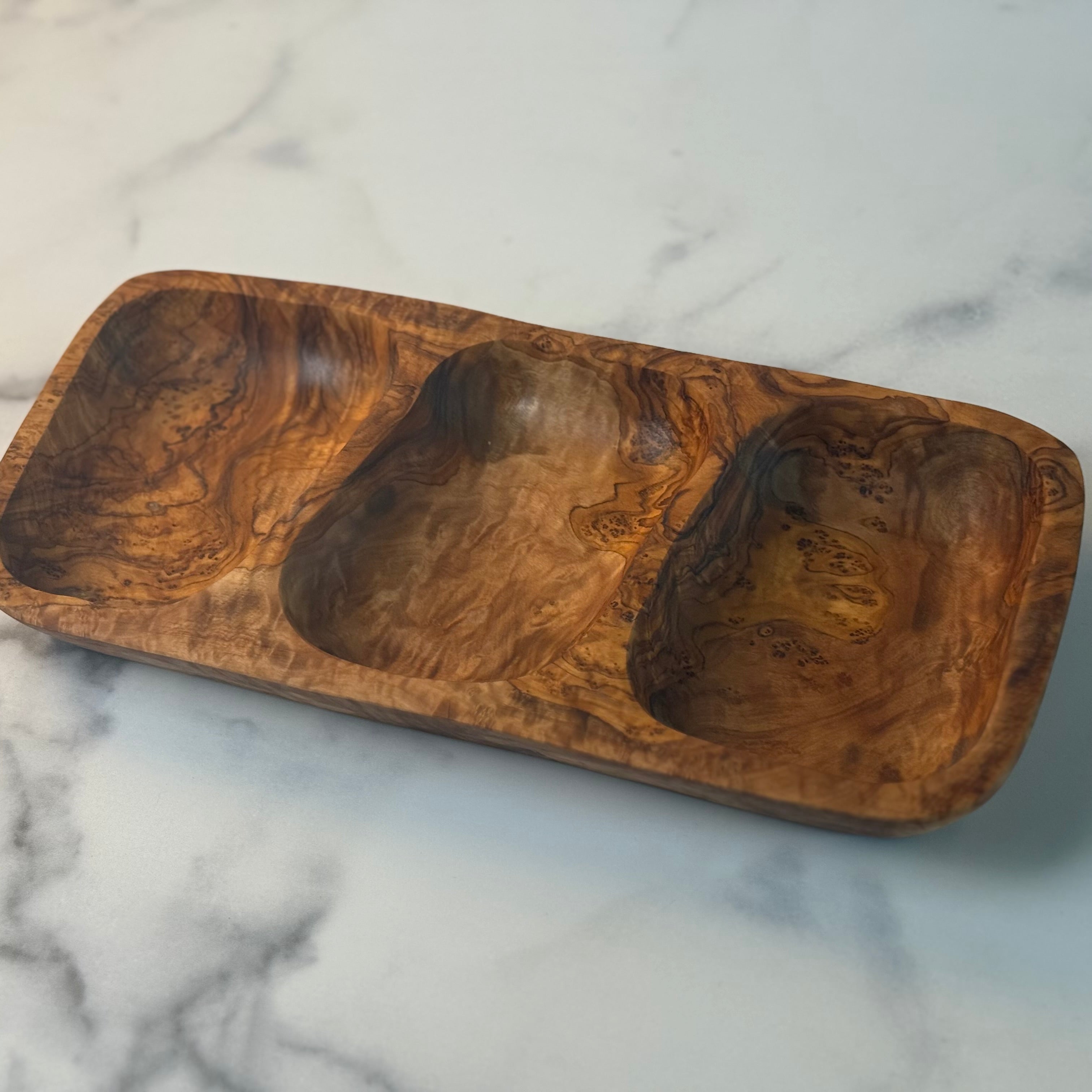 Handsome polished olivewood tray has shallow organically shaped depressions for holding appetizers. It is shown empty on a marble board.