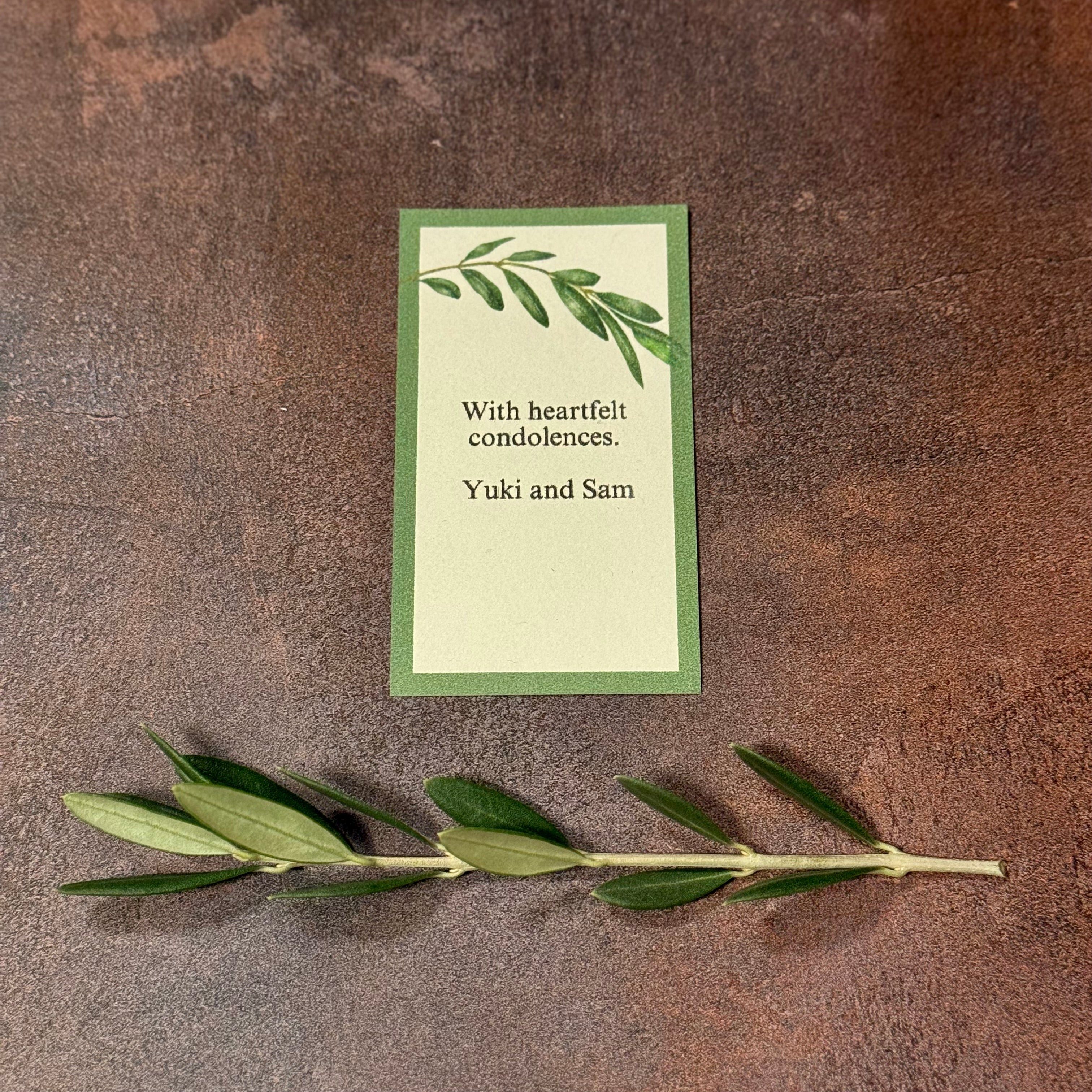 A single gift card is shown next to a small olive branch. The sentiment is an example of a personalized bereavement card, which says, "With heartfelt condolences, Yuki and Sam".