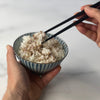 Donald's left hand holds a rice bowl full of Japanese short grain rice with Jacobsen Furikake sprinkles, and his right hand is shown picking up some of that rice with wooden chopsticks.