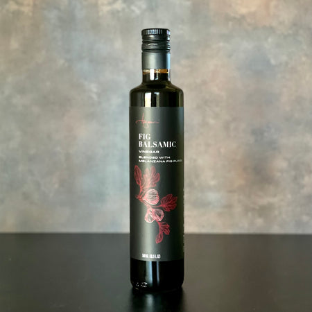 A single bottle of Melanzana Fig Balsamic Vinegar stands alone on a warmly inviting yet simple background