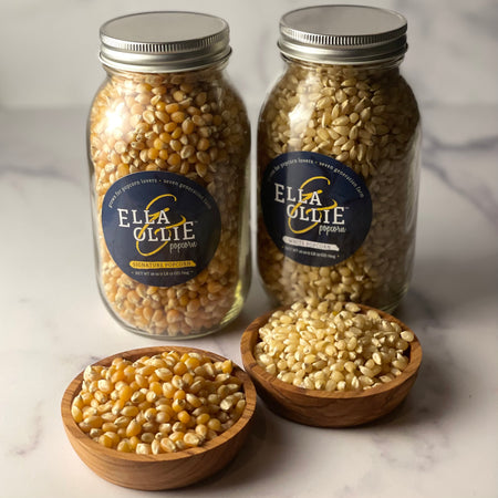 Signature popcorn with rounder larger kernels and white popcorn with narrower and smaller kernels are shown in little bowls in front of their respective jars.