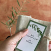 Liz holds a custom gift tag with a burlap bag behind it. an olive tree sapling is out of focus in the background