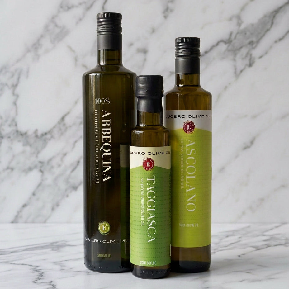 Three bottles of EVOO in a marble kitchen. A tall bottle of Arbequina, medium bottle of Ascolano, and a small bottle of Taggiasca.