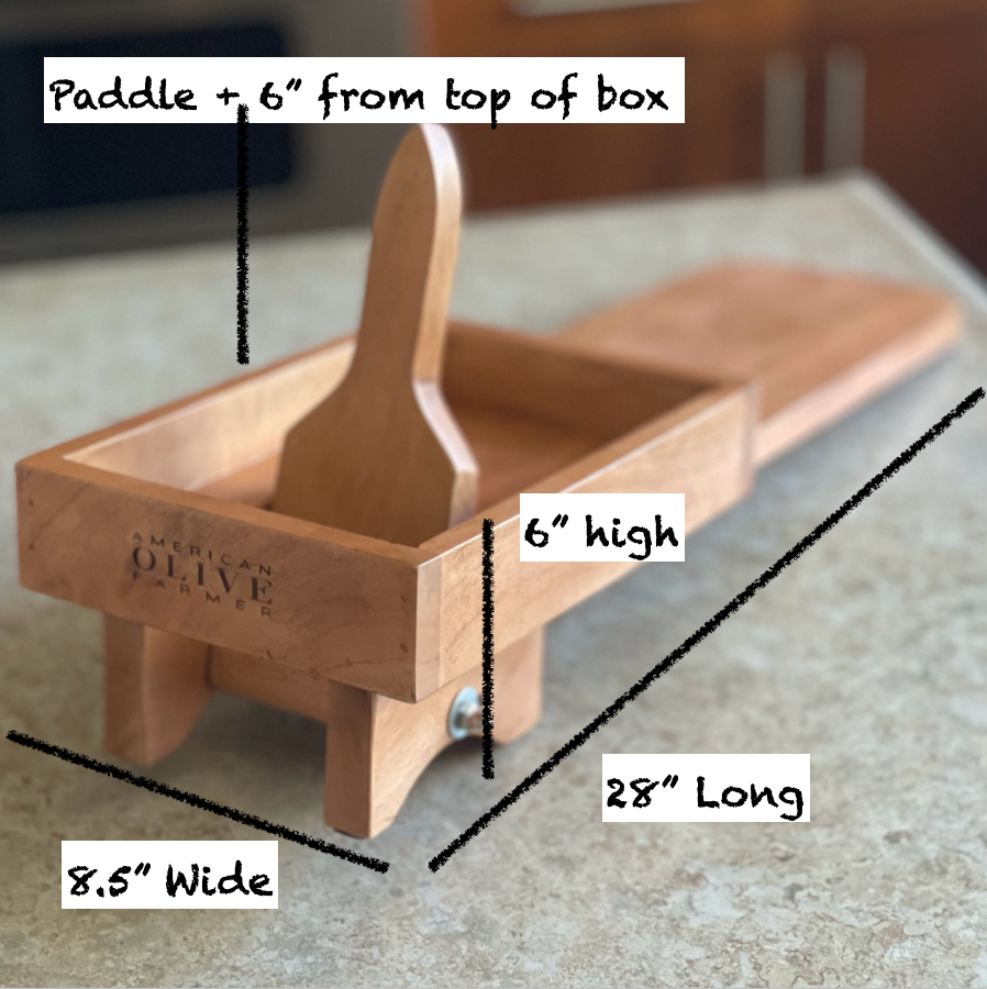 Close up image of the American Olive Farmer wooden olive crusher from the front. You can see the long back of the crusher seat gradually out of focus as it is further from the viewer