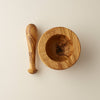 Overhead image of an olivewood pestle resting near a contemporary looking olivewood mortar. 