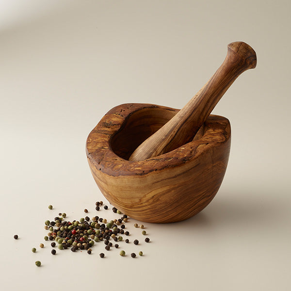 Rustic olivewood mortar with rough hewn swooping edges shown with pestle inside. 