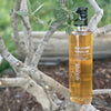 Amber colored white balsamic vinegar is stylishly printed glass bottle rests in the branches of a local olive tree.