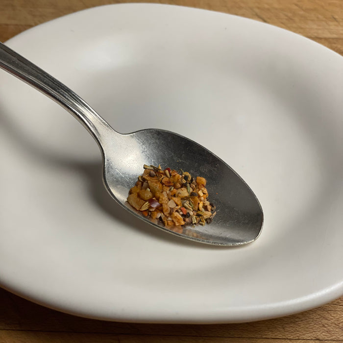 a close up image of the steak seasoning in a silver spoon on a white plate.