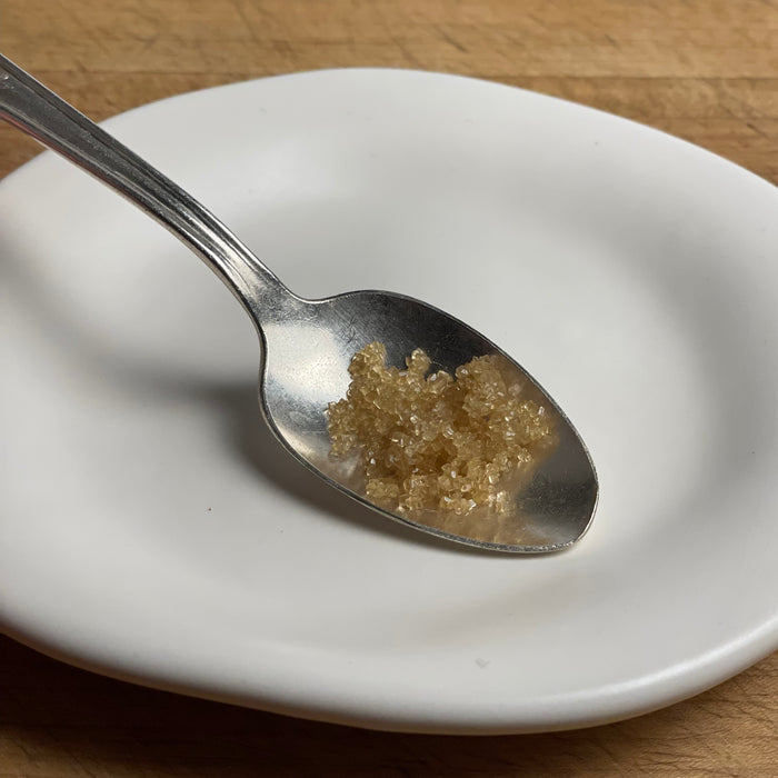 Smoked sugar crystals are shown in a silver spoon against a white plate on a cutting board