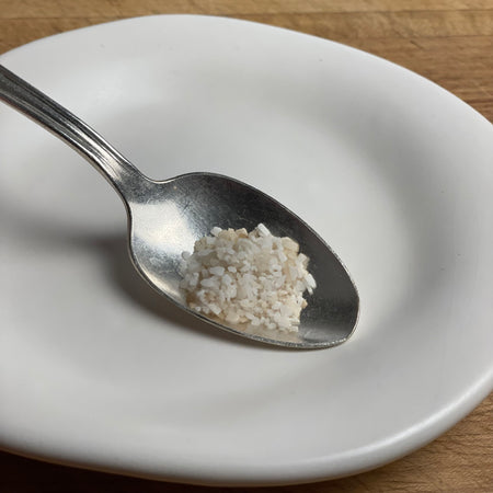 Coarse kosher salt which has been slow cold smoked is shown in a spoon on a  plate for contrast.