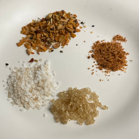 Four small piles of seasoning stand alone to show off texture:  seeds and grains for steak, sandy bits for poultry, crystals for sugar and coarse grains for salt.