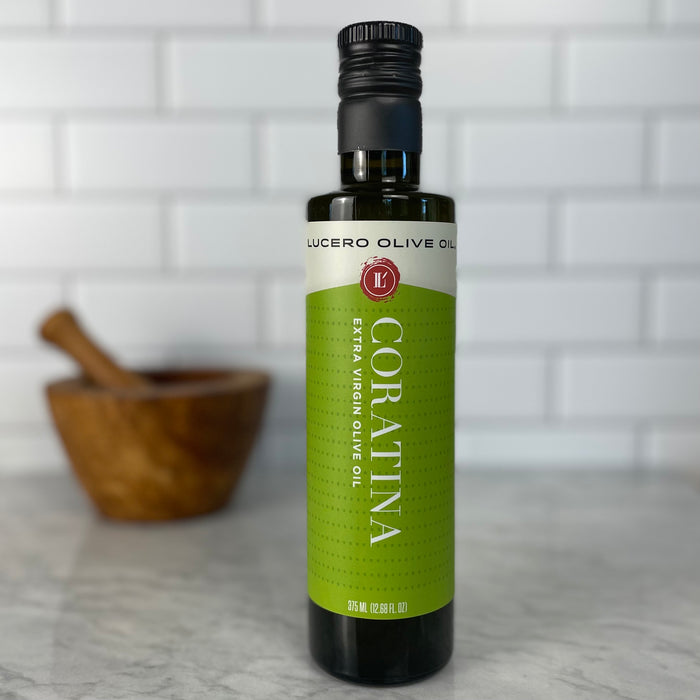 A bottle of Coratina EVOO in front of white tile sitting on white marble.