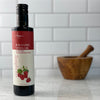 A bottle of Italian Raspberry Balsamic Vinegar rests on a white marble counter in front of a white tile backsplash.