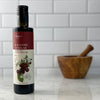 A bottle of Amarena Cherry Balsamic Vinegar rests on a white marble counter in front of a white tile background.