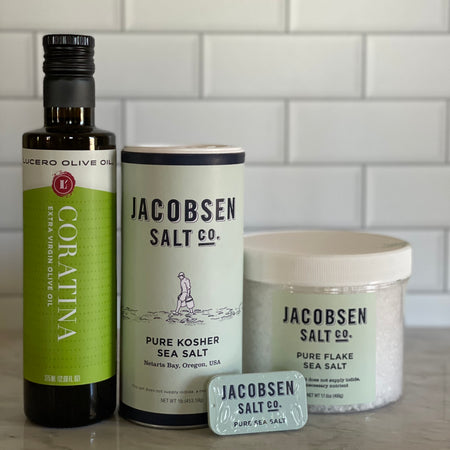 Coratina Extra Virgin Olive Oil is shown near Jacobsen's kosher, flake, and slider tin salts so that customers can compare size visually.