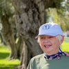 Liz's Mom wears the bright white AOF hat with the 100 year old Sevillano olive trees of Woodson Park in the background