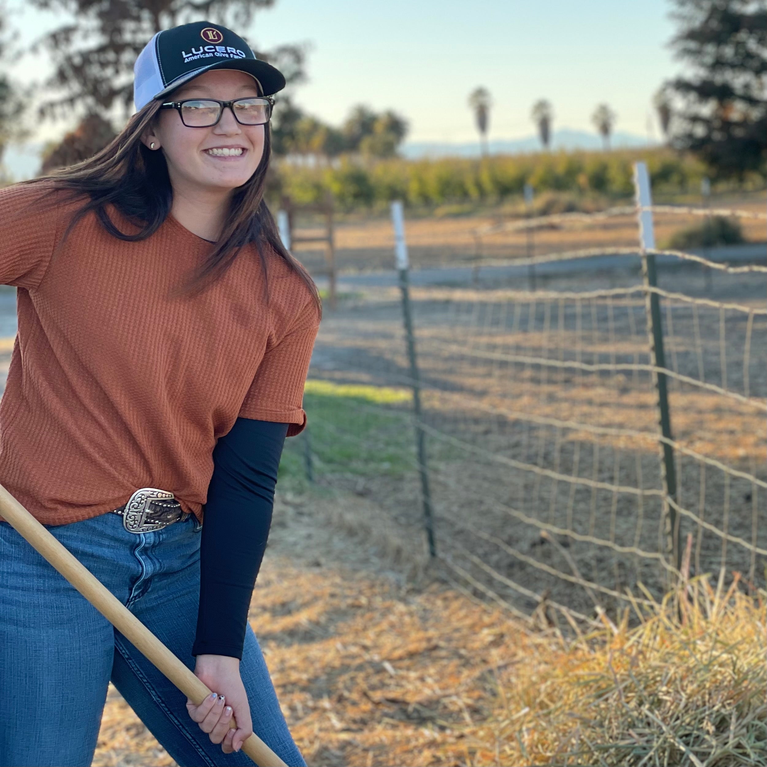 Young woman pitches hay while wearing her Lucero Trucker hat