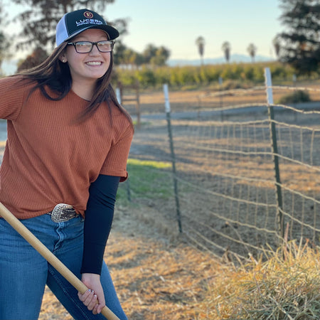 Young woman pitches hay while wearing her Lucero Trucker hat