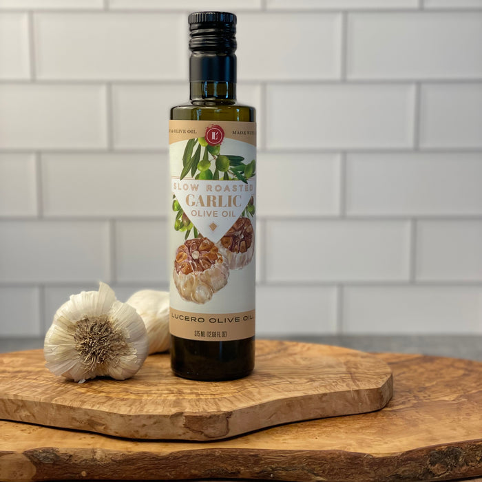 A bottle of slow roasted garlic olive oil is shown on a white marble counter with some bulbs of garlic in the background.  Edit alt text